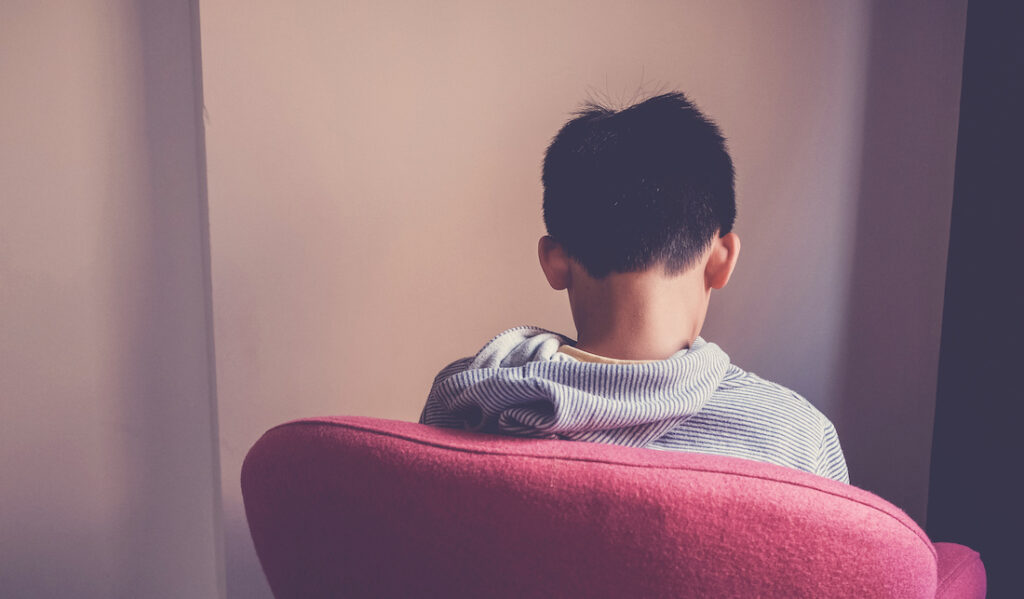 Sad preteen boy sitting alone in chair facing wall, depressed,introvert, autism awareness, children mental health,psychology teen autism spectrum disorder, social distancing, self isolation concept Sad preteen boy sitting alone in chair facing wall, depressed,introvert, autism awareness, children mental health,psychology teen autism spectrum disorder, social distancing, self isolation concept